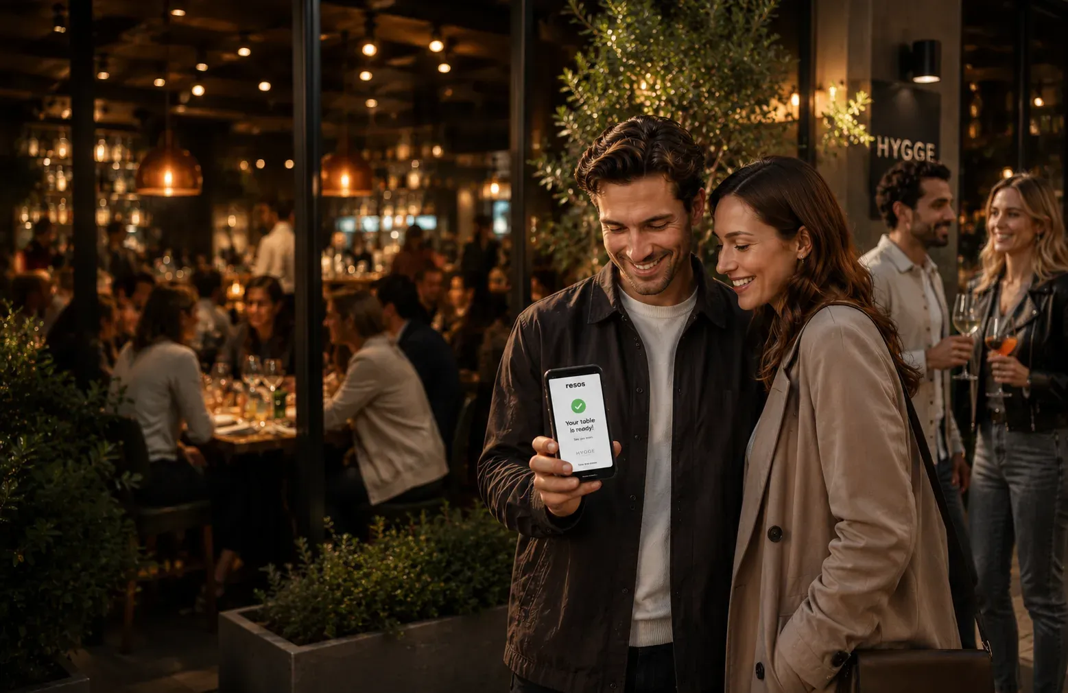 Couple at a restaurant looking at a phone showing a Resos table-ready waitlist notification