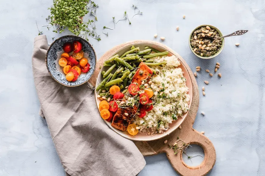 Healthy food served on 3 plates: beans, tomatoes, salmon, cuscus, and other vegetables.