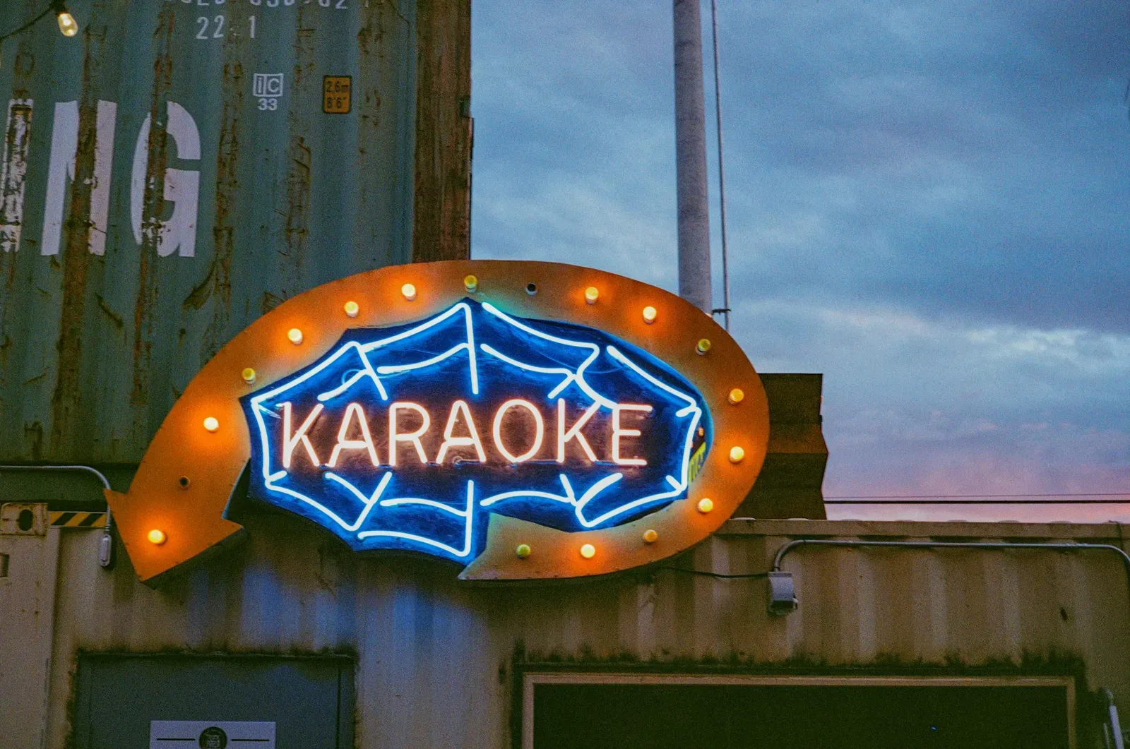 Neon karaoke sign glowing outside a bar at dusk